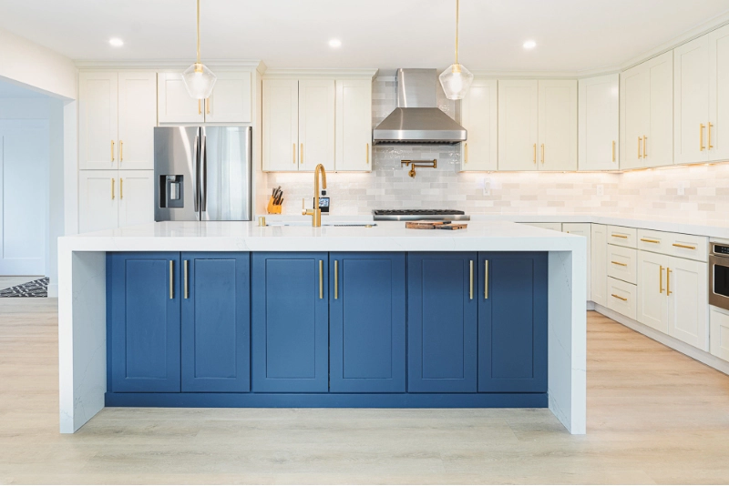 A modern kitchen features a large island with blue cabinets and gold handles, white countertops, and pendant lights.