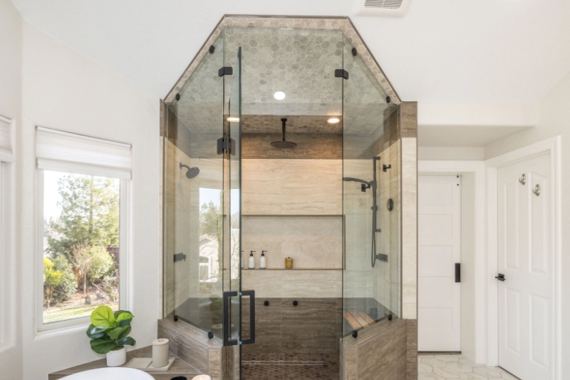 A modern bathroom features a glass-enclosed shower with wooden accents, a rain showerhead, a handheld shower nozzle, and built-in shelving.