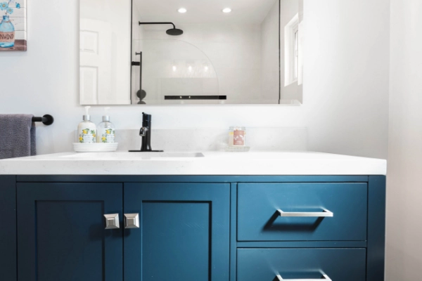 A modern bathroom with a blue vanity, white countertop, and black faucet.