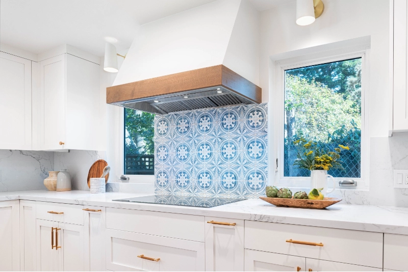 A modern kitchen with white cabinets, a marble countertop, and a blue patterned tile backsplash showcases the luxury home remodel.