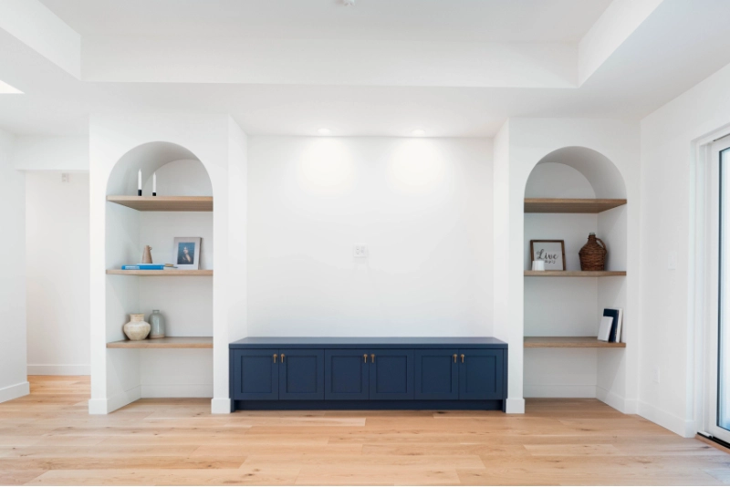 A minimalist living room featuring built-in shelves with decorative items, a blue storage cabinet below, and wooden flooring.