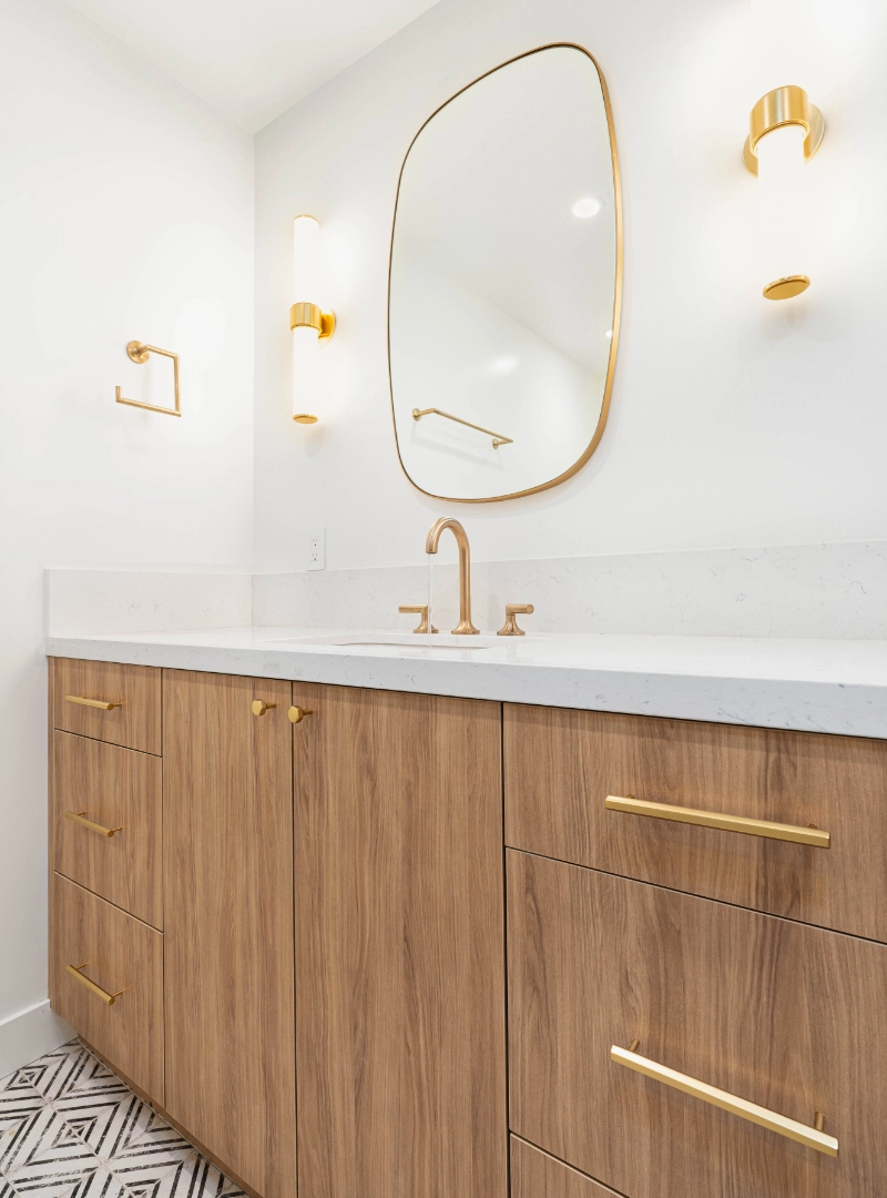 Modern bathroom with light wood vanity, gold hardware, and fixtures.