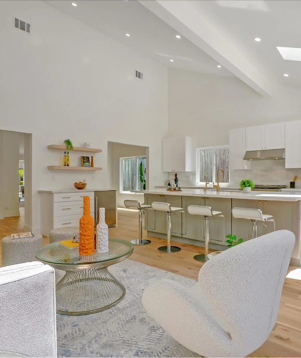 Modern, open-concept living space featuring a kitchen with white cabinets and a breakfast bar with stools.