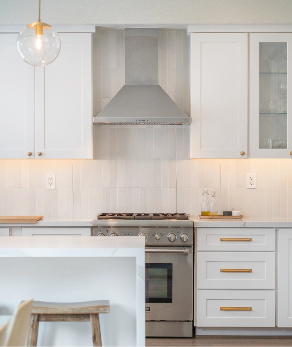 Experience the epitome of elegance in this modern kitchen, featuring white cabinets, a stainless steel oven and range hood, a white tile backsplash, and a single hanging pendant light.