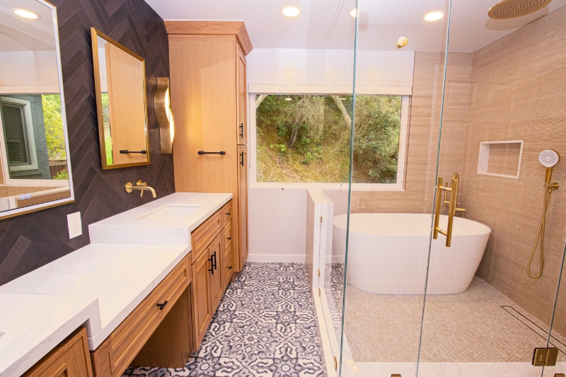 Modern bathroom featuring a double vanity, wall-mounted faucets, a freestanding tub, a glass-enclosed shower, patterned floor tiles, and a large window with a view of greenery.