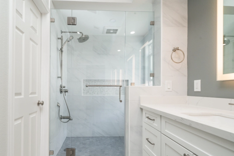 A modern Regency bathroom remodel features a glass-enclosed shower, a white vanity with drawers and sink, a towel ring on the wall, and a grey tiled floor.