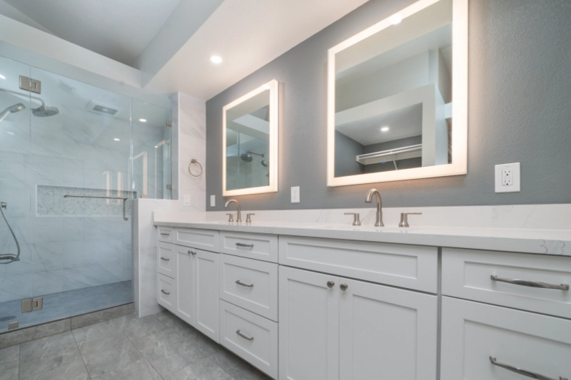 A Regency Bathroom Remodel showcases a modern bathroom featuring a large glass-enclosed shower, dual sinks with mirrors, and white cabinetry with silver fixtures under bright lighting.