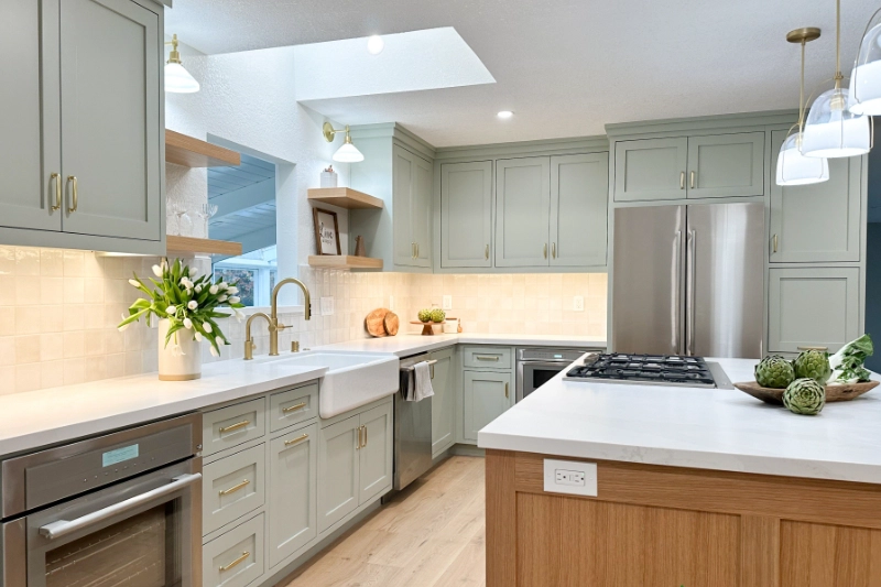 Modern kitchen with light gray cabinets, white countertops, stainless steel appliances, and a large central island with a gas cooktop. Skylight and overhead lights illuminate the space in this San Mateo Full Home Remodel & Addition.